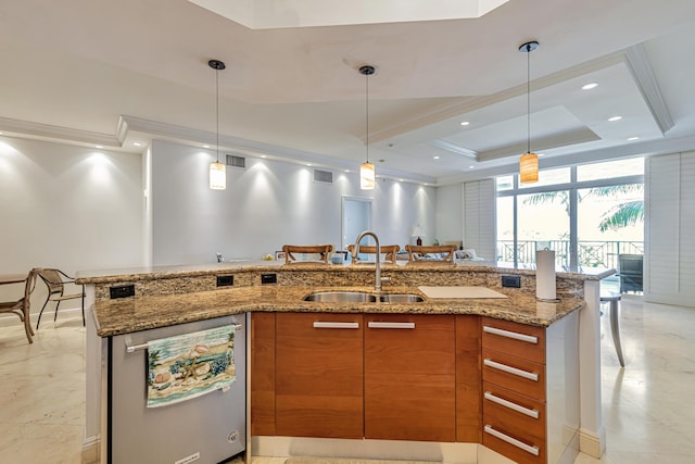 kitchen with a sink, brown cabinetry, stainless steel dishwasher, a raised ceiling, and hanging light fixtures