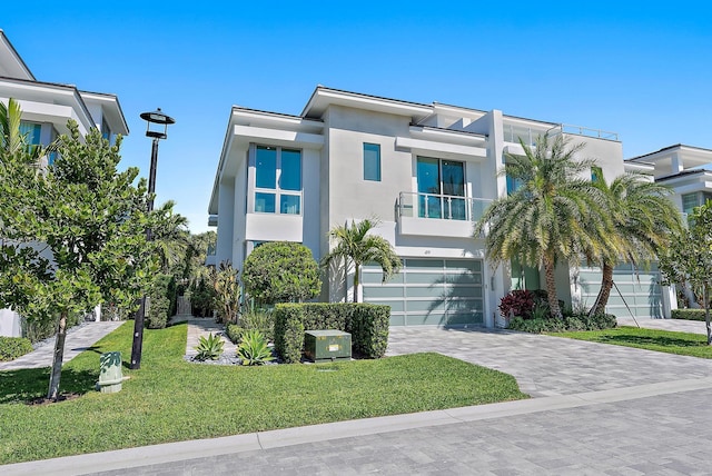 view of front of house with decorative driveway, stucco siding, a front yard, a balcony, and a garage