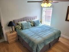 bedroom featuring light wood-type flooring, a wall unit AC, baseboards, and a ceiling fan