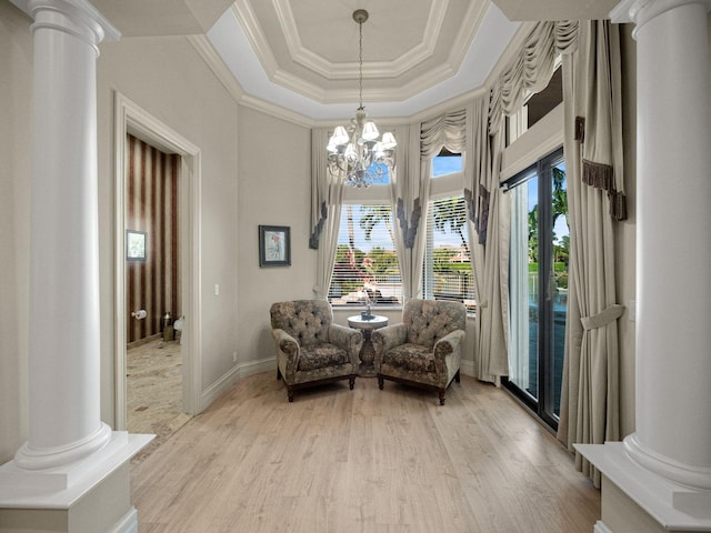 sitting room with light wood-style flooring, a notable chandelier, ornamental molding, a raised ceiling, and ornate columns