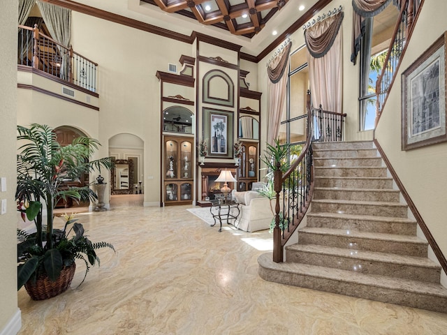 staircase featuring a high ceiling, coffered ceiling, marble finish floor, a lit fireplace, and ornamental molding