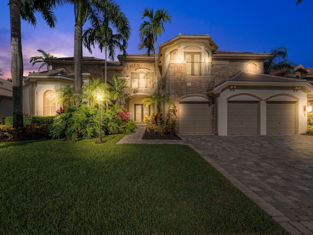 mediterranean / spanish house with decorative driveway, stucco siding, a lawn, a balcony, and stone siding