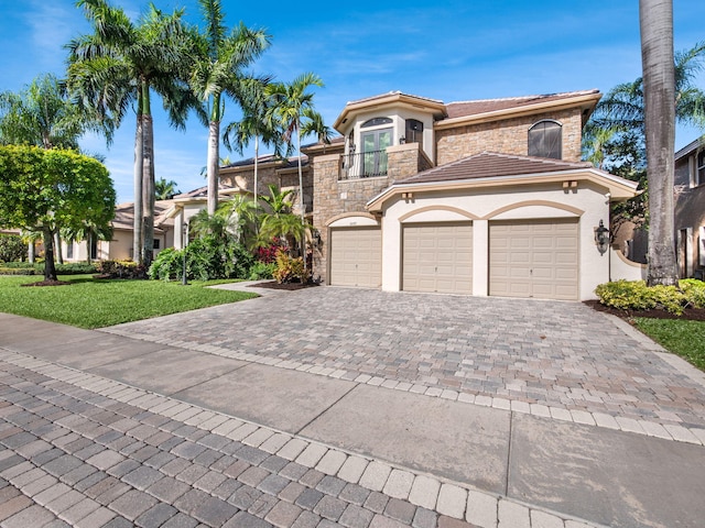 view of front of house featuring decorative driveway, stucco siding, a front yard, a balcony, and stone siding