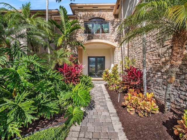 doorway to property featuring a balcony, stucco siding, stone siding, and french doors