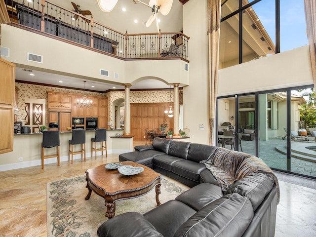 living room with decorative columns, visible vents, baseboards, and ceiling fan with notable chandelier