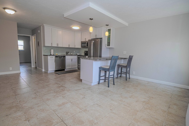 kitchen with a peninsula, a breakfast bar, white cabinetry, appliances with stainless steel finishes, and tasteful backsplash