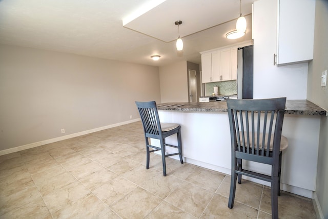 kitchen with a peninsula, a breakfast bar, white cabinetry, fridge, and backsplash