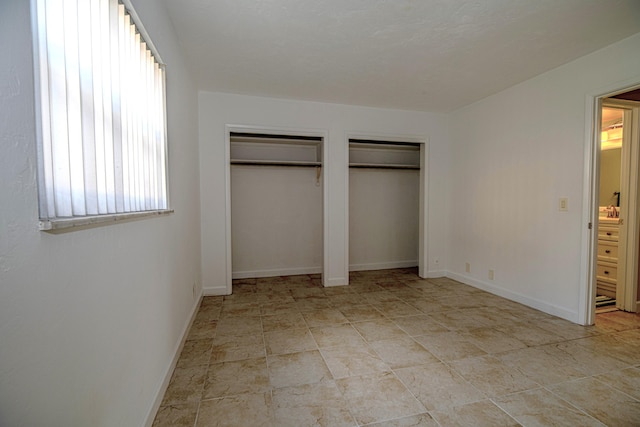 unfurnished bedroom with two closets and baseboards