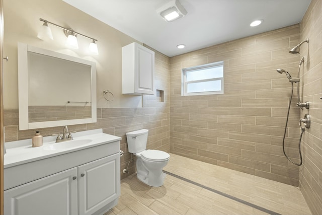 bathroom featuring vanity, a tile shower, toilet, and tile walls