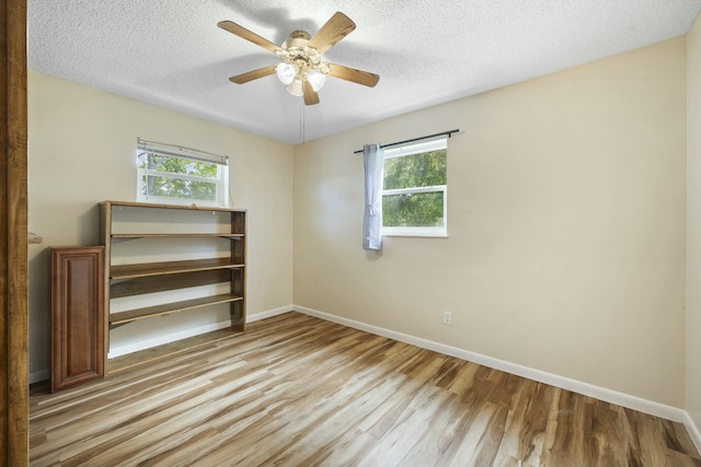 empty room with a textured ceiling, light wood-type flooring, and baseboards