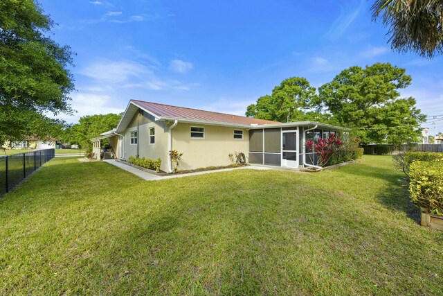 rear view of property featuring metal roof, a lawn, a fenced backyard, and a sunroom