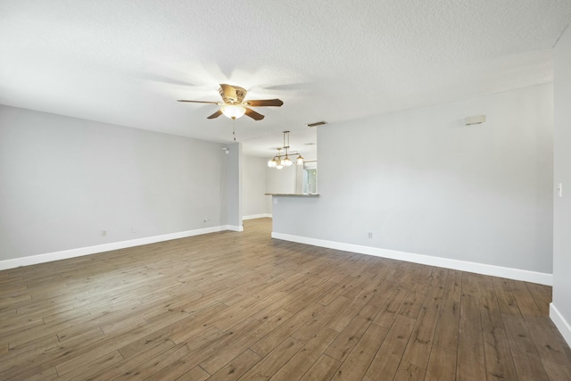 unfurnished room with ceiling fan with notable chandelier, a textured ceiling, baseboards, and wood finished floors