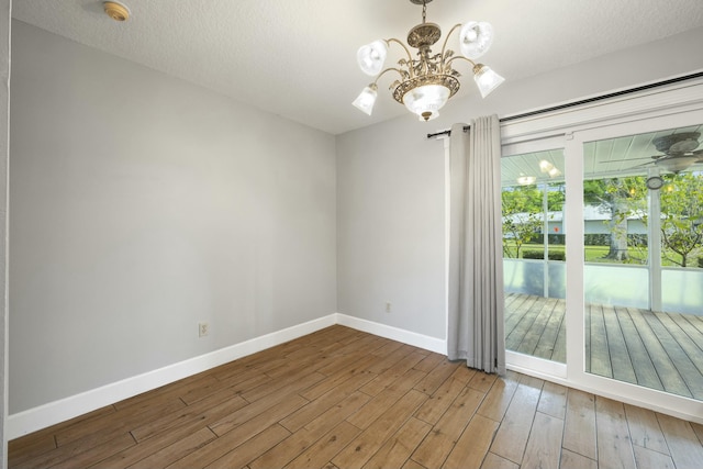 empty room featuring a textured ceiling, baseboards, a chandelier, and wood finished floors