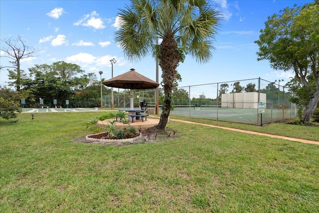 view of property's community featuring a tennis court, fence, a gazebo, and a lawn