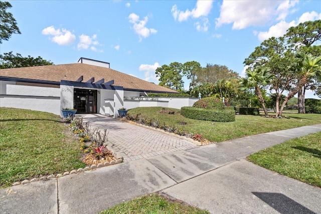 view of front of home featuring concrete driveway, roof with shingles, a front yard, and stucco siding