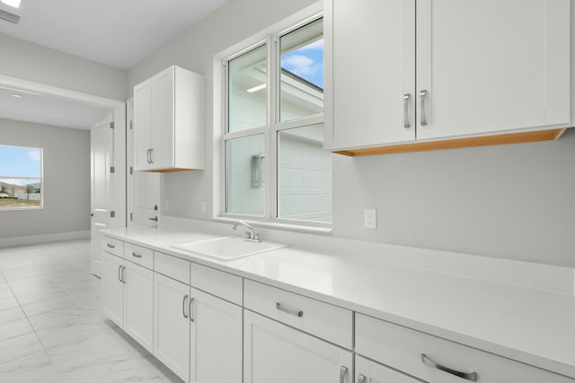 kitchen with a sink, visible vents, white cabinetry, marble finish floor, and light countertops