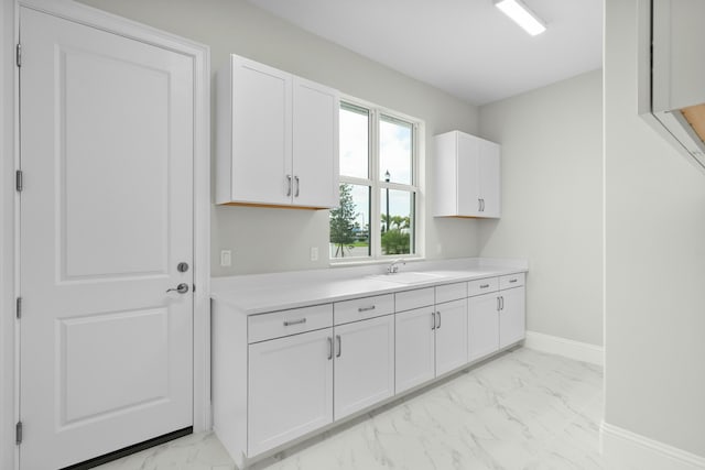 kitchen with marble finish floor, light countertops, white cabinets, a sink, and baseboards