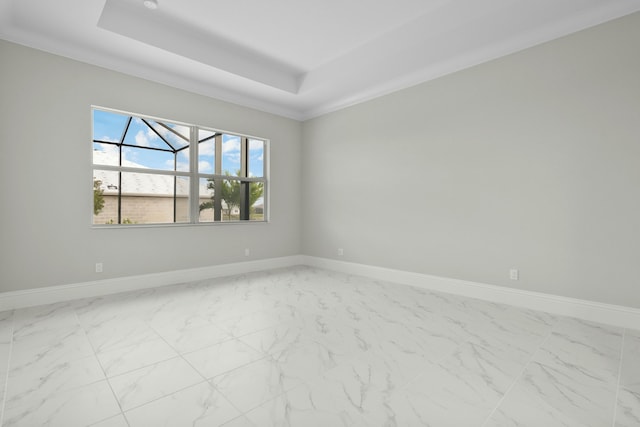 empty room with marble finish floor, a tray ceiling, and baseboards