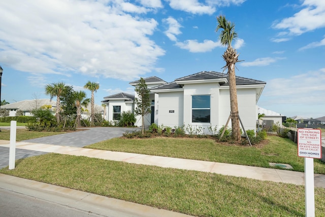 view of front of property featuring a tile roof, a front lawn, decorative driveway, and stucco siding