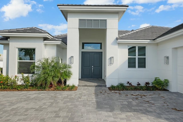 view of exterior entry with a garage, a tile roof, and stucco siding