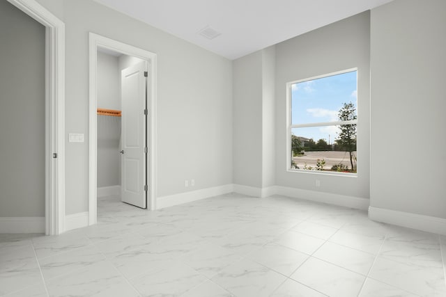 unfurnished bedroom with marble finish floor, baseboards, and a walk in closet