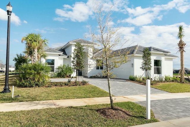 view of front of house featuring a garage, a tile roof, decorative driveway, a front lawn, and stucco siding