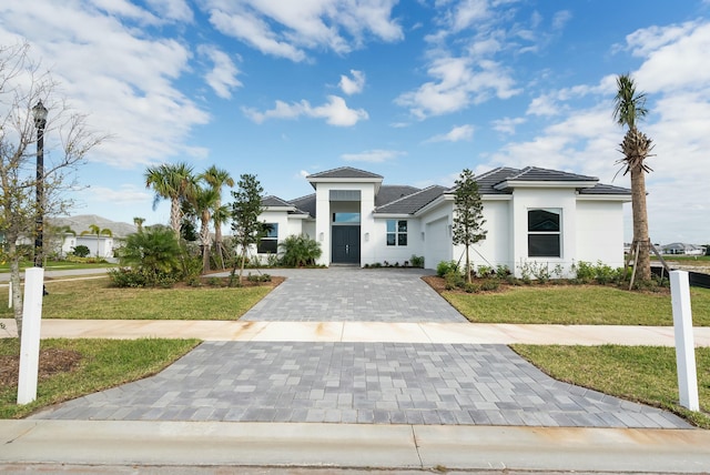 prairie-style house featuring an attached garage, a tiled roof, decorative driveway, stucco siding, and a front yard