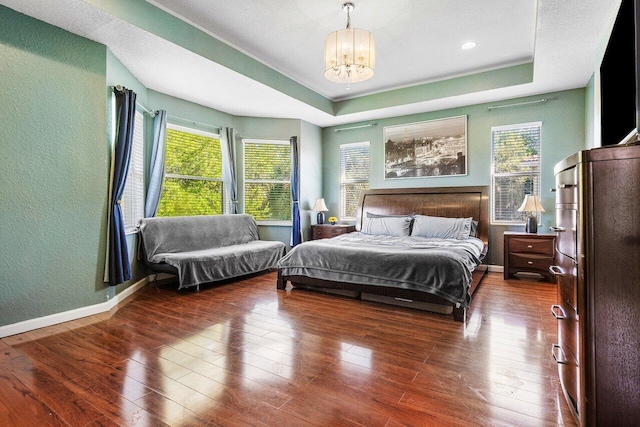 bedroom with hardwood / wood-style flooring, multiple windows, and a raised ceiling