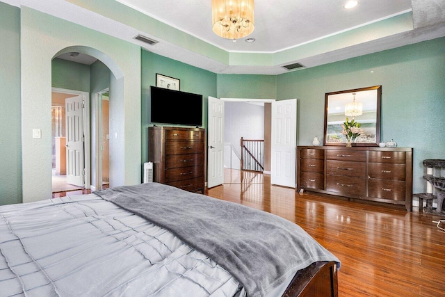 bedroom with a chandelier, a tray ceiling, wood finished floors, and visible vents