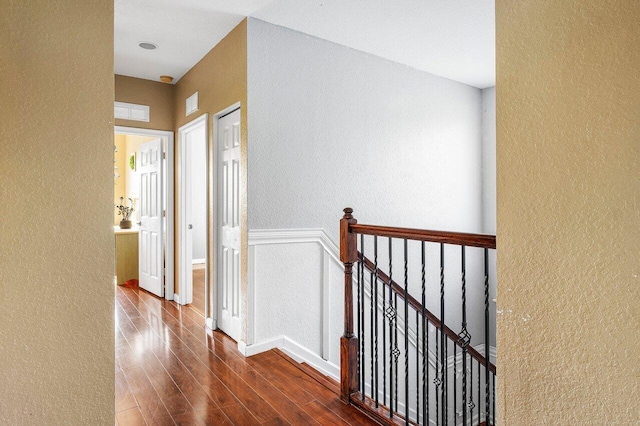 hall with dark wood-style floors, a textured wall, visible vents, and an upstairs landing