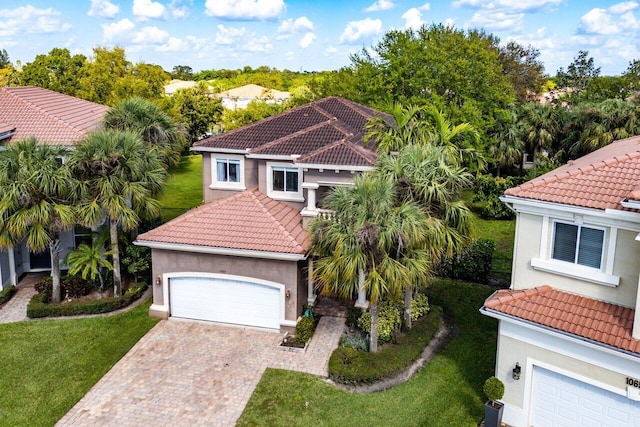 mediterranean / spanish home with decorative driveway, a tiled roof, a front lawn, and stucco siding