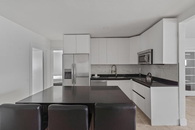 kitchen with decorative backsplash, white cabinets, dark countertops, stainless steel appliances, and a sink