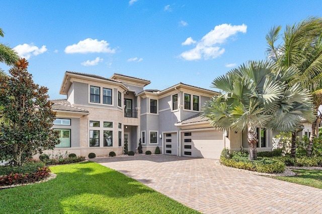 prairie-style home featuring a garage, a front lawn, decorative driveway, and stucco siding