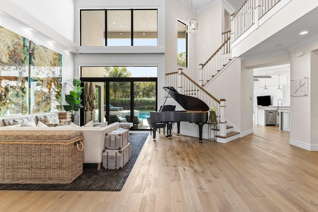 living area with crown molding, a towering ceiling, wood finished floors, baseboards, and stairs