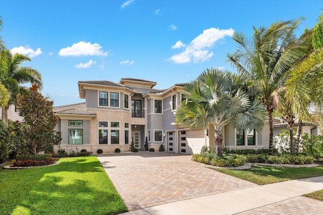 prairie-style house with a front yard, decorative driveway, an attached garage, and stucco siding