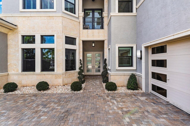 view of exterior entry featuring french doors, a balcony, and stucco siding