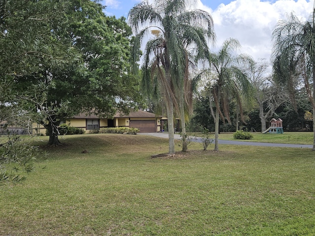 exterior space with an attached garage, a playground, driveway, and a front lawn