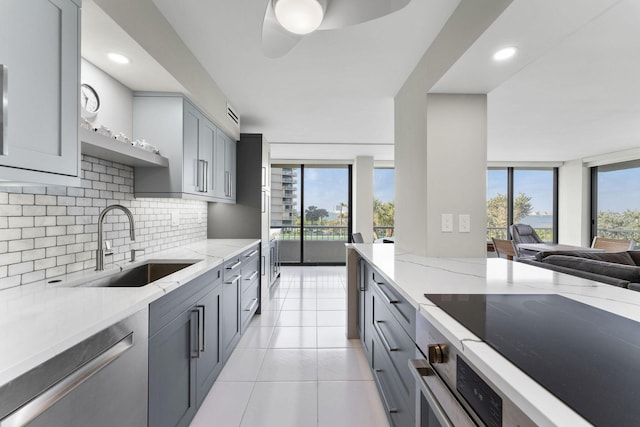 kitchen with backsplash, light stone countertops, gray cabinets, stainless steel dishwasher, and a sink