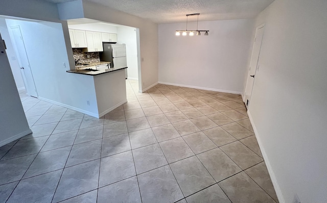 kitchen with dark countertops, freestanding refrigerator, white cabinetry, decorative light fixtures, and backsplash