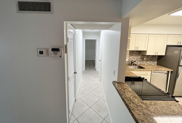 interior space with backsplash, visible vents, a sink, light tile patterned floors, and dishwashing machine