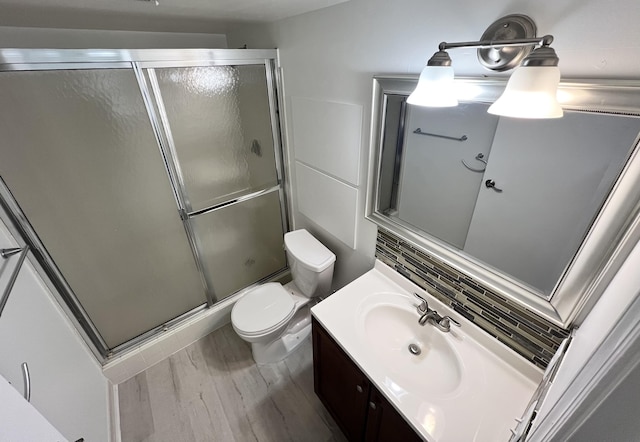 bathroom featuring vanity, wood finished floors, toilet, tasteful backsplash, and a shower stall
