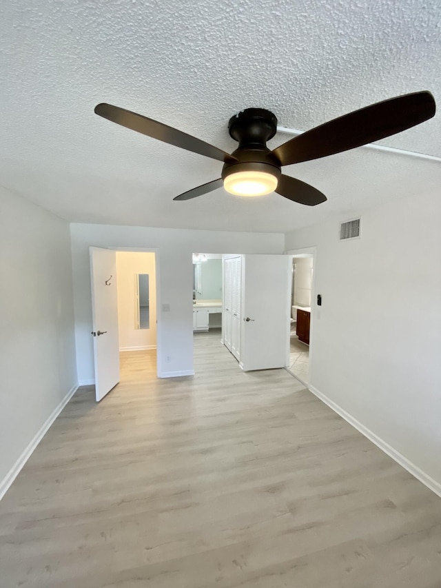 interior space with baseboards, light wood finished floors, a textured ceiling, and visible vents