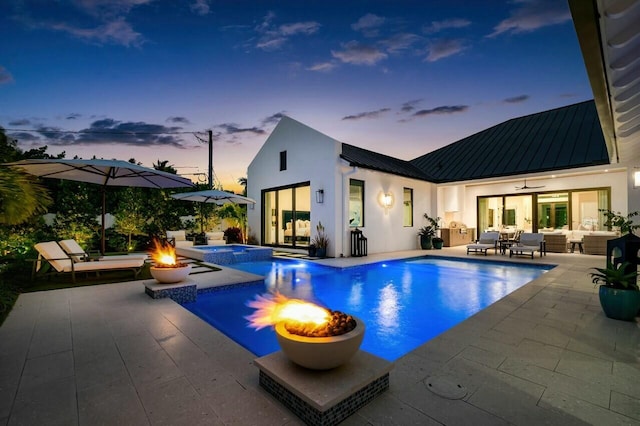 pool at dusk featuring a patio area, an outdoor living space with a fire pit, and a pool with connected hot tub