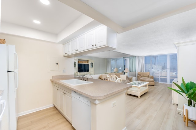 kitchen featuring a peninsula, white appliances, a sink, white cabinets, and light wood-style floors