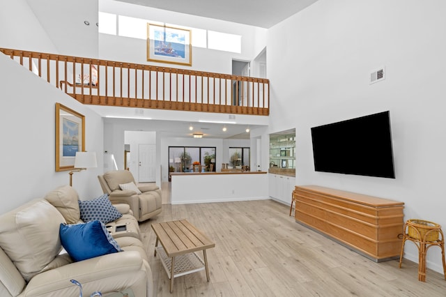 living area with light wood-type flooring, a healthy amount of sunlight, a high ceiling, and visible vents