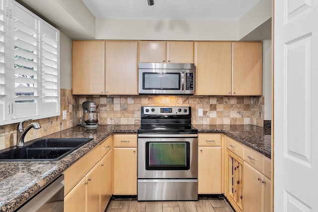 kitchen with stainless steel appliances, light brown cabinets, a sink, and decorative backsplash