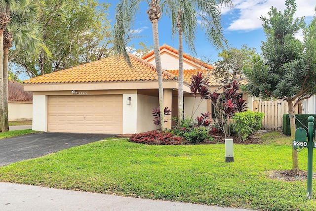 mediterranean / spanish home with aphalt driveway, an attached garage, fence, a front lawn, and stucco siding