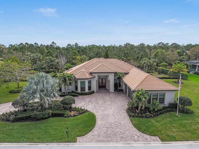 mediterranean / spanish-style home with decorative driveway, a front yard, a tile roof, and stucco siding