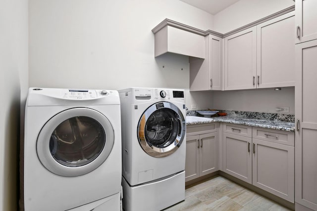 clothes washing area featuring light wood-style flooring, washing machine and clothes dryer, and cabinet space