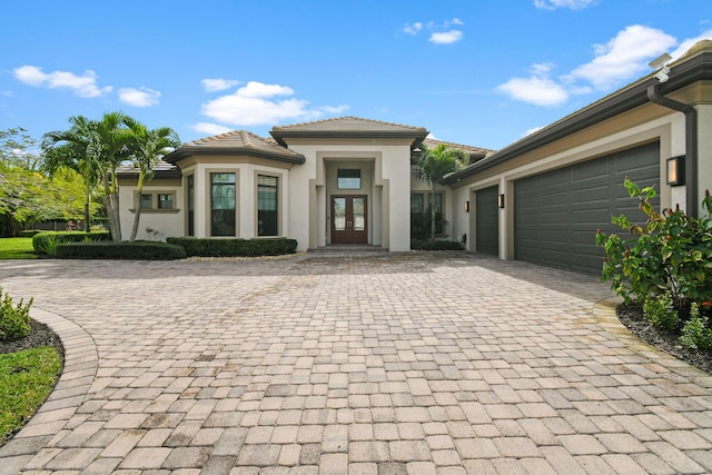 prairie-style house with an attached garage, stucco siding, decorative driveway, and french doors